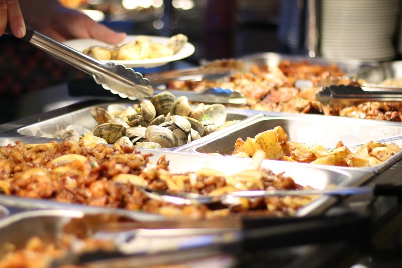 Guest filling a plate at the buffet line, with pans of clams, stir-fried dishes and potatoes