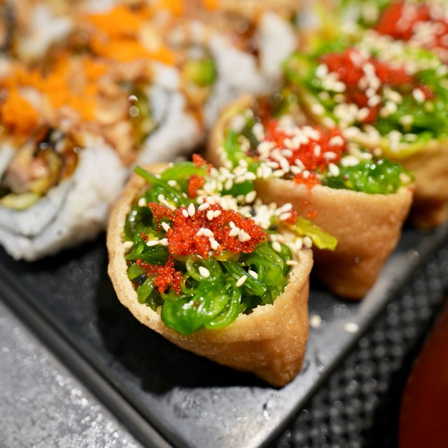 Seaweed salad inari topped with roe and sesame, next to sushi rolls